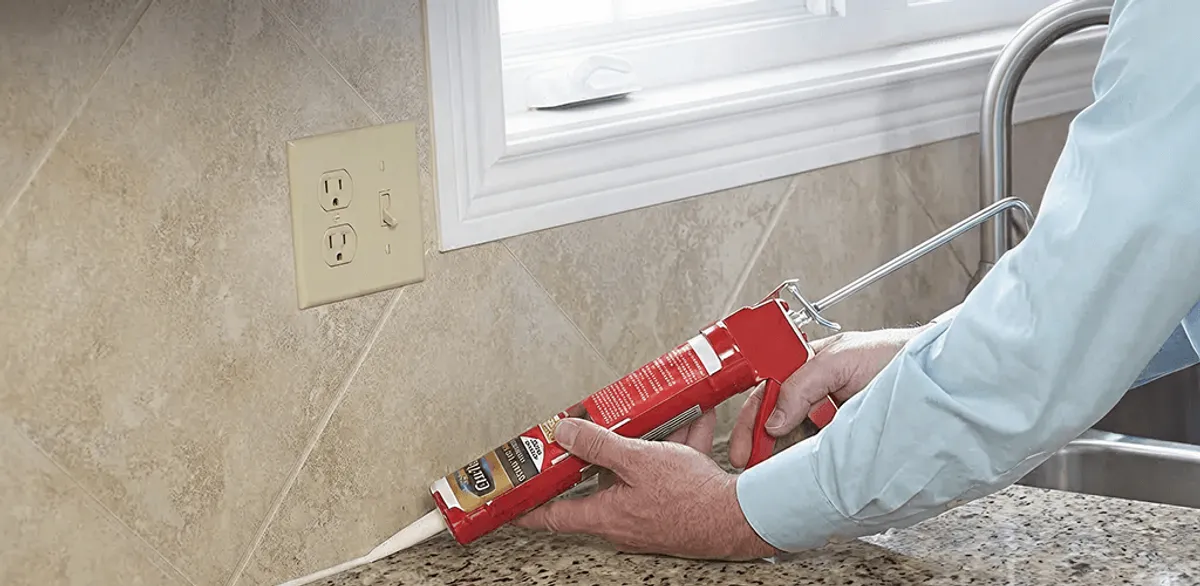 Handyman applying caulk along a kitchen backsplash and countertop seam in Jackson, MS