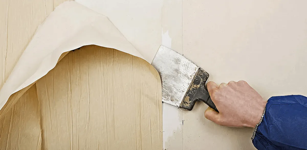 Handyman removing wallpaper with a scraper for wall preparation in Jackson, MS